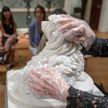 Accessibility. For visitors who are blind or partially sighted touch tours are available. A woman wearing plastic gloves touches a plaster sculpture. 