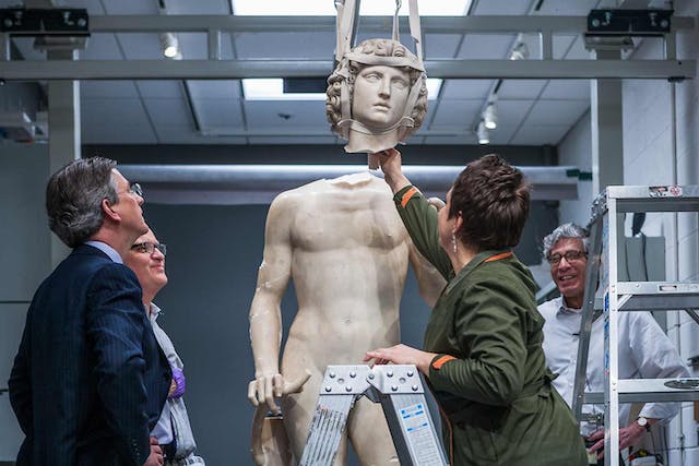 Met staff lowering down the detached head of a marble statue back onto its body