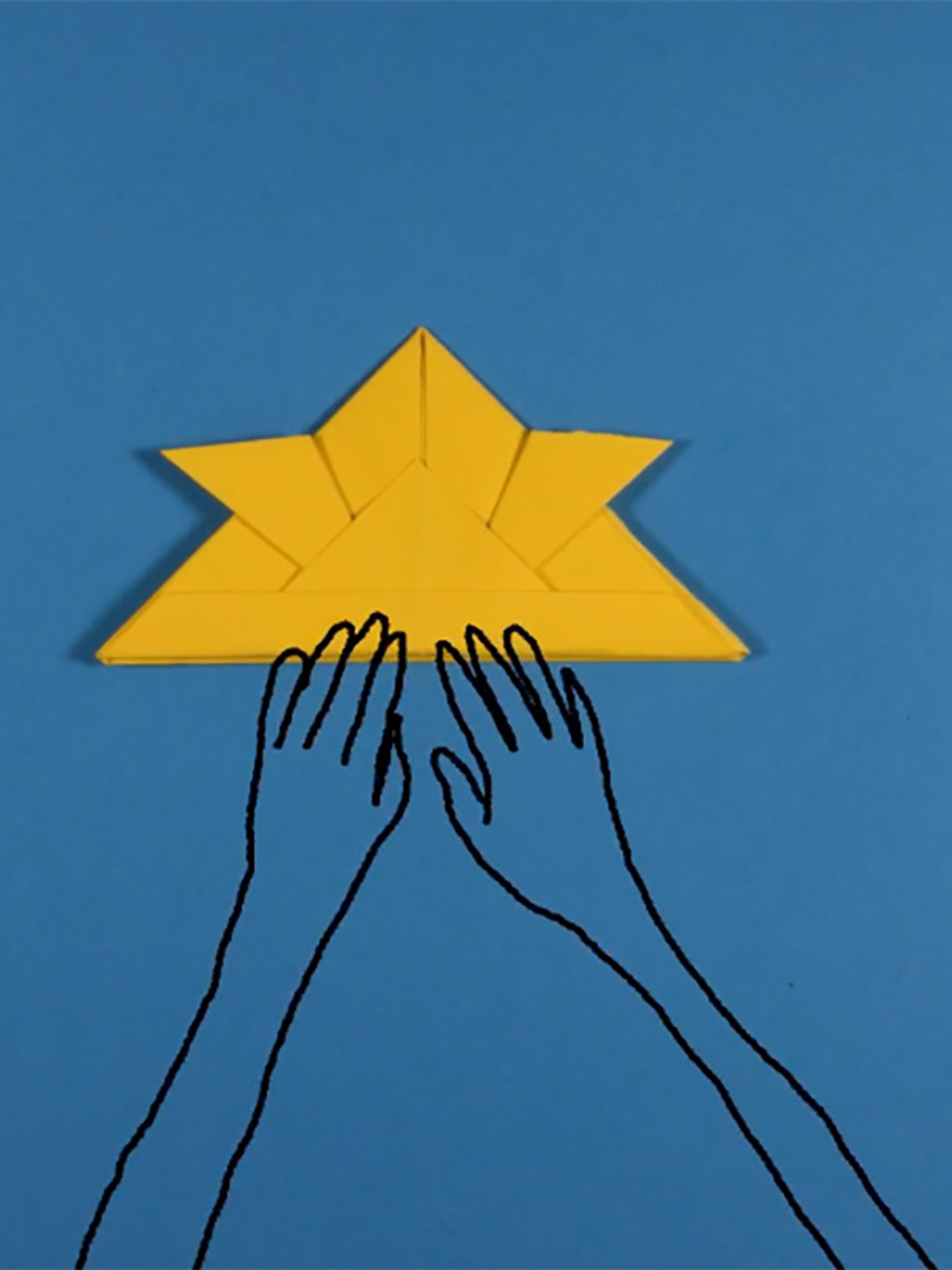 Animated hands work to fold a yellow oragami helmet placed on a blue background.