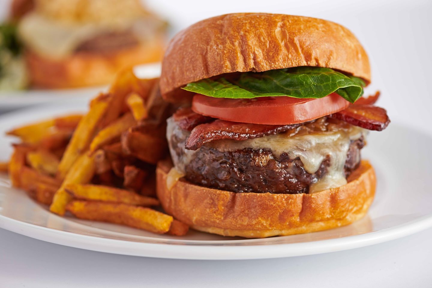 A cheeseburger with lettuce and tomatoes sits on a white plate with a side of french fries. 